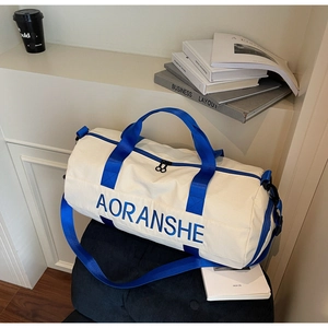 Close-up of cream travel bag with blue handles and detachable shoulder strap on a chair