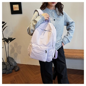 Détail du sac à dos en nylon violet clair montrant la poche avant zippée et le logo rond
