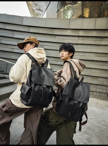 Outdoor view of dual black leather backpacks featuring flap drawstring and side pockets