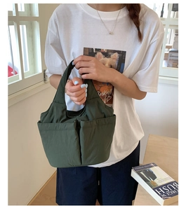 Detail of dark green nylon tote bag featuring front pockets and handheld strap for daily use