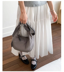 Close-up of grey nylon crossbody bag with a zipped pocket and woven zipper pull