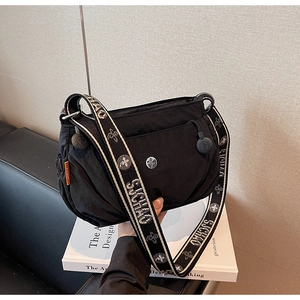 Detail of black nylon crossbody bag with jacquard strap and brand logo on a white book