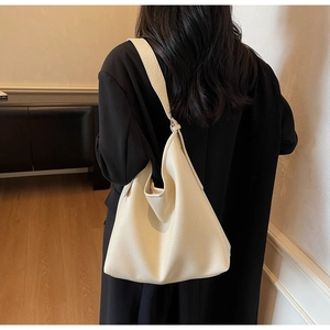 Detail of off-white hobo bag with litchi texture and wide strap on model back