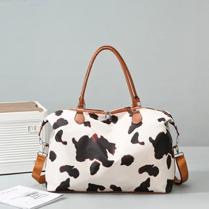 Detail of cow print travel bag with brown leather handles and adjustable side buckles