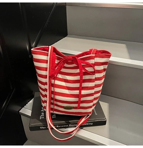 Detail of red and white striped knit tote bag with bow accent and metal brand plaque