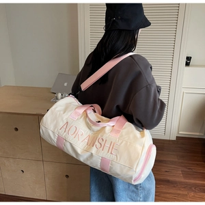 Detail of embroidered pink logo on cream canvas travel bag with adjustable strap