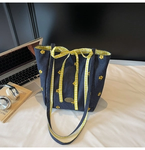 Detail of blue denim tote bag with yellow floral embroidery and a plaid bow ribbon