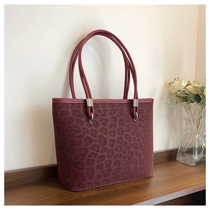 Dettaglio della borsa shopper bordeaux leopardata con hardware in metallo su legno