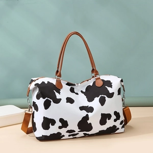 Detail of travel bag with cow print pattern, brown woven shoulder strap and metal zipper
