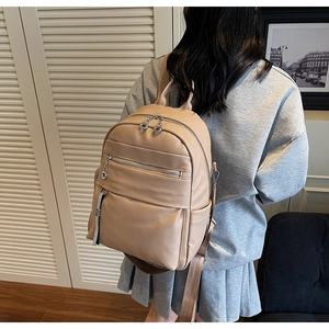 Close-up of beige litchi grain leather backpack with silver zippers on a model back