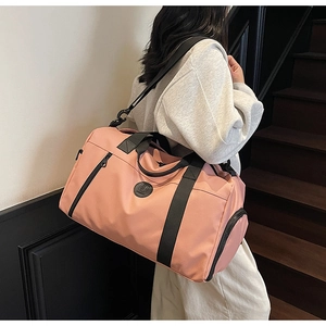 Detail view of pink travel bag with black straps worn by a model in an indoor setting