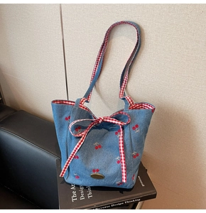 Detail of blue denim shoulder bag featuring red cherry embroidery and a checkered bow