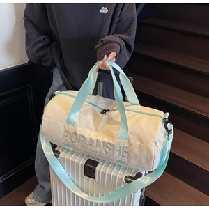 Close-up of a cream and mint green travel duffel bag on a white suitcase