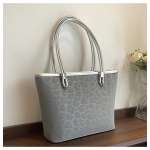 Vista dettagliata della borsa tote leopardata grigia con manici argento su tavolo in legno