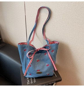 Detail of blue denim tote bag with cherry embroidery and red checkered bow ribbons