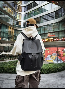 Outdoor view of a black faux leather backpack with drawstring closure and flap cover