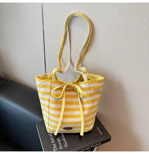 Detail of yellow and white striped canvas tote bag with ribbon bow and metal logo