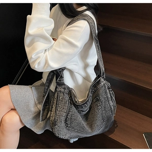 Detail of a large denim tote bag featuring a decorative bow knot on the wide shoulder strap