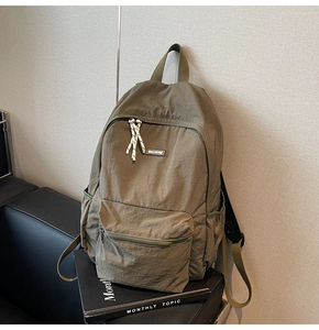 Detail view of dark green nylon backpack showing front zip pocket and woven zipper pulls