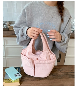 Detailed view of pink multi-pocket nylon handbag held by a model in a modern kitchen setting