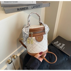 Detail of white quilted bucket bag with brown leather trim and decorative silk handle scarf