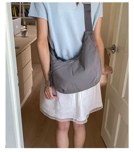 Detailed view of a grey nylon half-moon crossbody bag with a woven zipper pull and logo