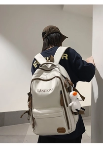 Detail of cream backpack with brown accents featuring TIANFLONG logo and duck pendant