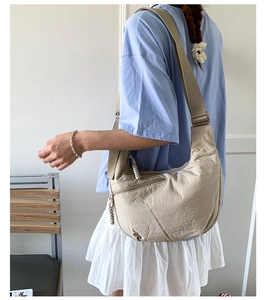 Detail of light beige nylon crescent bag featuring adjustable strap worn by model