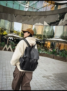 Outdoor shot of a black vintage flap backpack with drawstring closure and side pockets