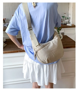 Detail of beige crescent crossbody bag with adjustable wide strap and front zipper pocket