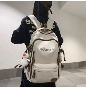 Rear view of an off-white canvas backpack with brown straps and a cute duck pendant