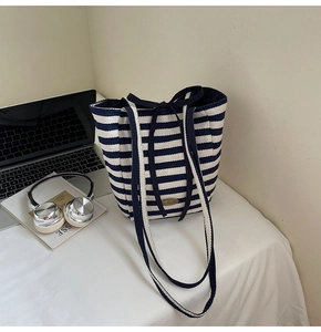 Detail of navy blue striped canvas tote bag with decorative bow and handmade metal logo tag