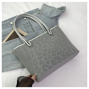 Dettaglio della borsa tote leopardata grigia con manici in metallo argento su denim