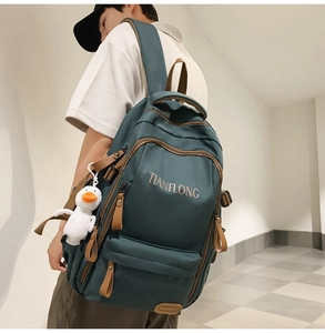 Close-up of teal canvas backpack with micro-fiber leather details and white duck pendant