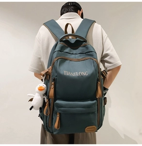 Detail of dark green nylon backpack featuring brown leather accents and a cute duck pendant