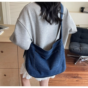 Detail of a large dark blue denim crossbody bag with wide shoulder strap on a model