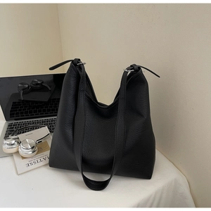 Detail of black pebbled leather tote bag with adjustable strap next to a laptop