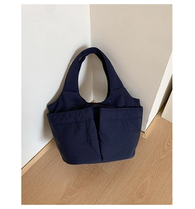 Detail of navy blue multi-pocket nylon tote bag leaning against a white wall