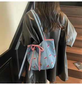 Detail of blue denim tote bag featuring red cherry embroidery and a checkered bow accent