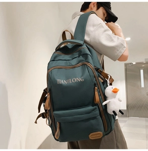Detail view of large dark green backpack with brown trim and small duck plush accessory