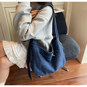 Close-up of large blue denim tote bag with visible stitching and wide strap on model