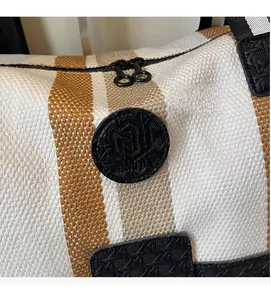 Detail of striped canvas travel bag featuring black leather logo and dual zipper closure