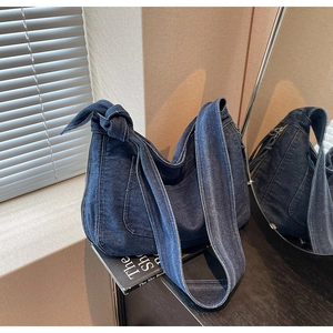 Detail of blue denim hobo bag featuring contrast stitching and a knotted shoulder strap