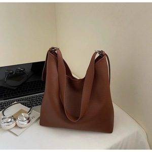 Detail of coffee brown lychee grain leather tote bag with wide strap on a desk