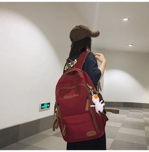 Detail view of large burgundy canvas backpack with multiple pockets and cute duck pendant