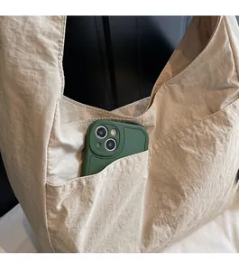 Detail of beige nylon hobo bag featuring a functional front pocket holding a smartphone