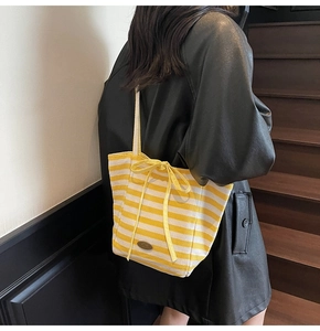 Model view of a yellow and white striped canvas tote bag with a bow and shoulder strap