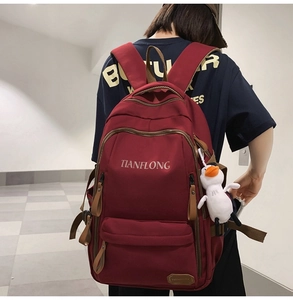 Detail view of burgundy nylon backpack with multiple compartments and white duck pendant