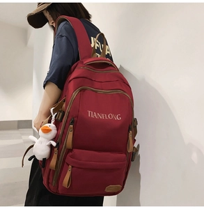 Deep red waterproof backpack with a cute white duck pendant shown on a model