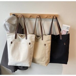 Detailed row of canvas tote bags in white, beige, and black with leather straps